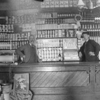 Photograph of two men behind a counter in a store.