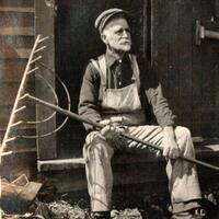 Seated man in overalls holding rake