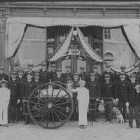Two rows of uniformed men around a horse drawn but horse-less fire engine