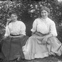 Two women seated near a bush