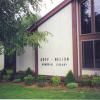 Photo of flower bed outside the front of the library with small bushes and flowers. Goff-Nelson sign on side of building also shown.